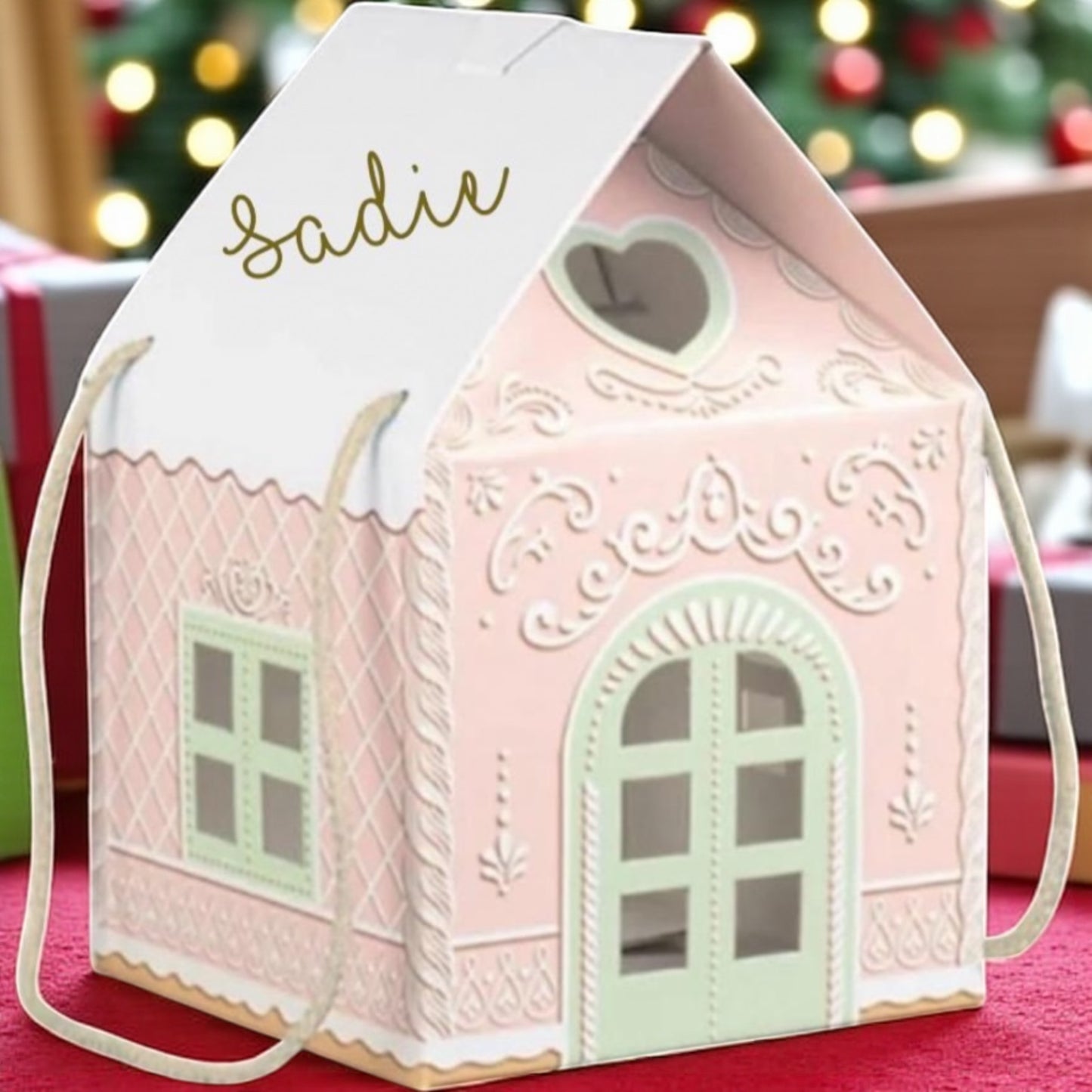Pink house-shaped gift bag with 'Sadie' on top, against a blurred festive background.