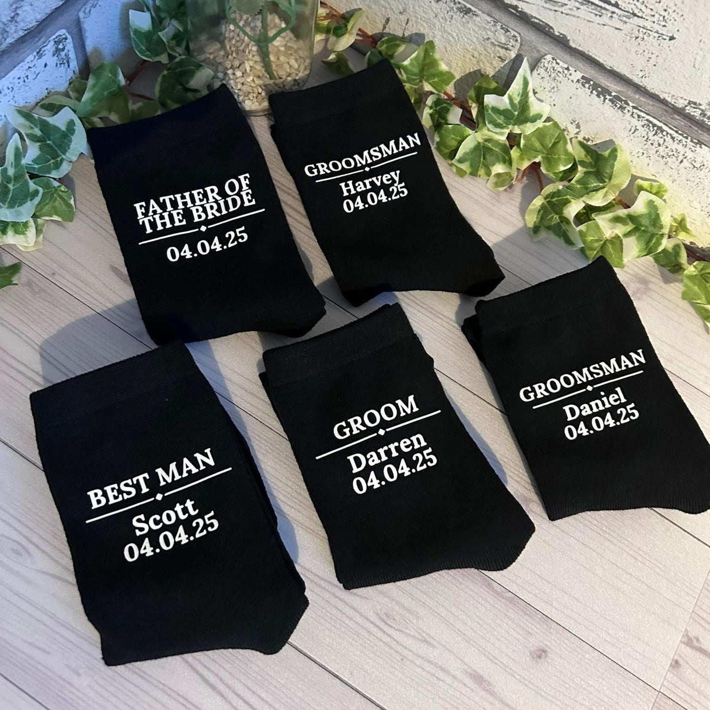 Black socks with personalized text on a wooden surface with greenery