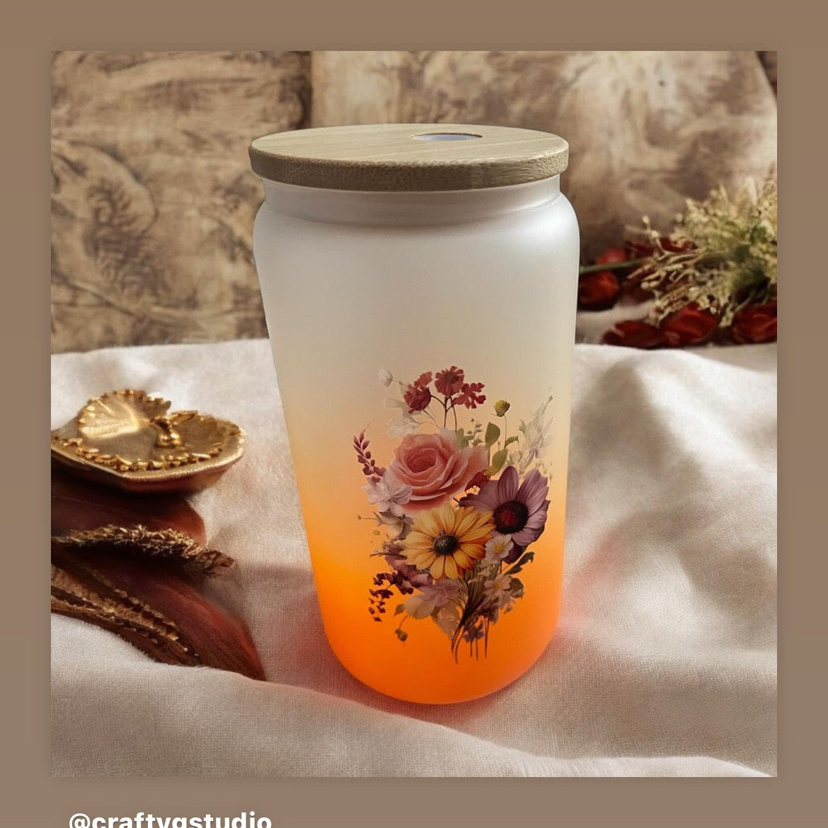 A 16oz tumbler with a clear glass body and an ombre design that transitions from a light to dark color, featuring a floral pattern at the bottom. It includes a glass straw.