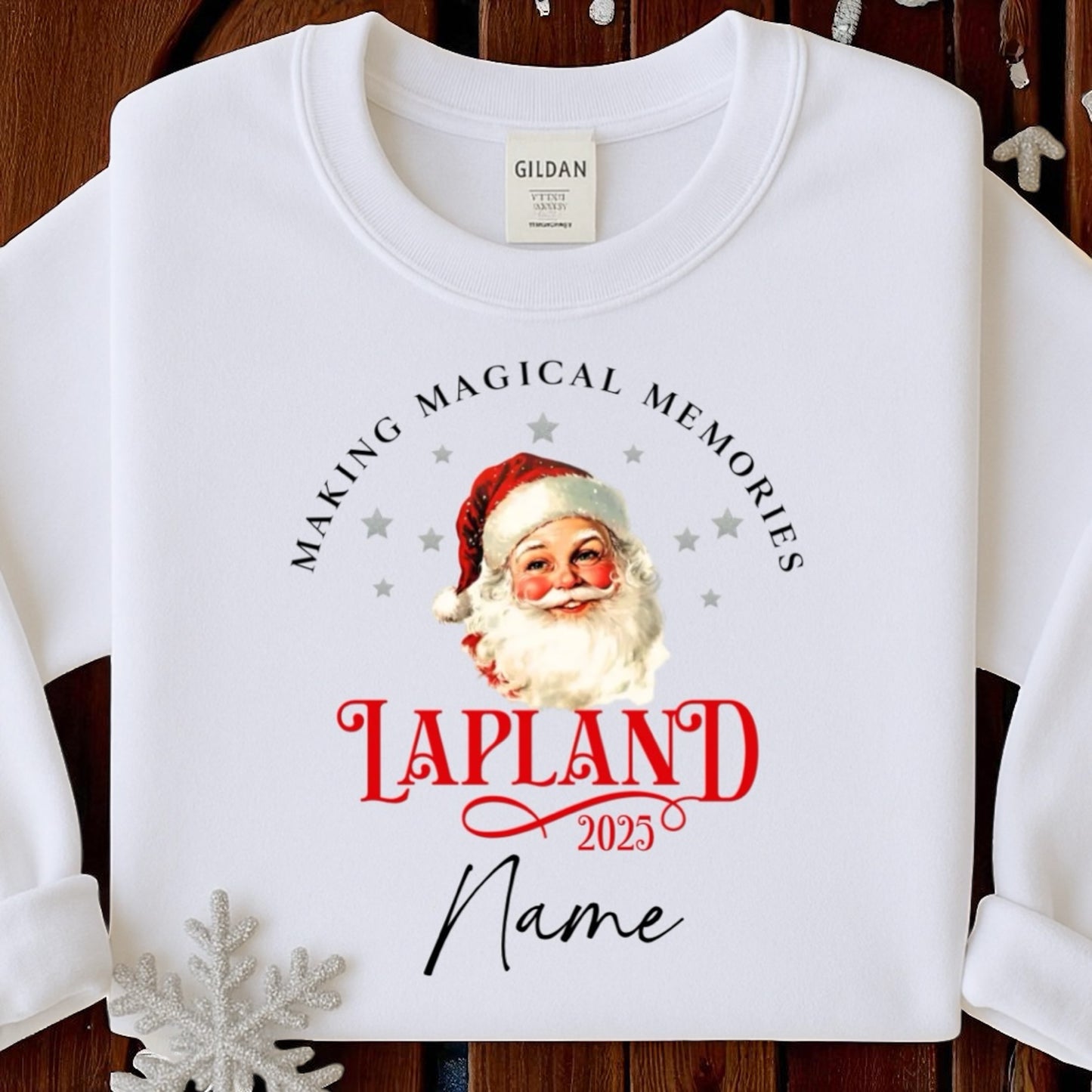 White sweatshirt with Santa Claus graphic and text 'Making Magical Memories Lapland 2025' on a wooden surface.