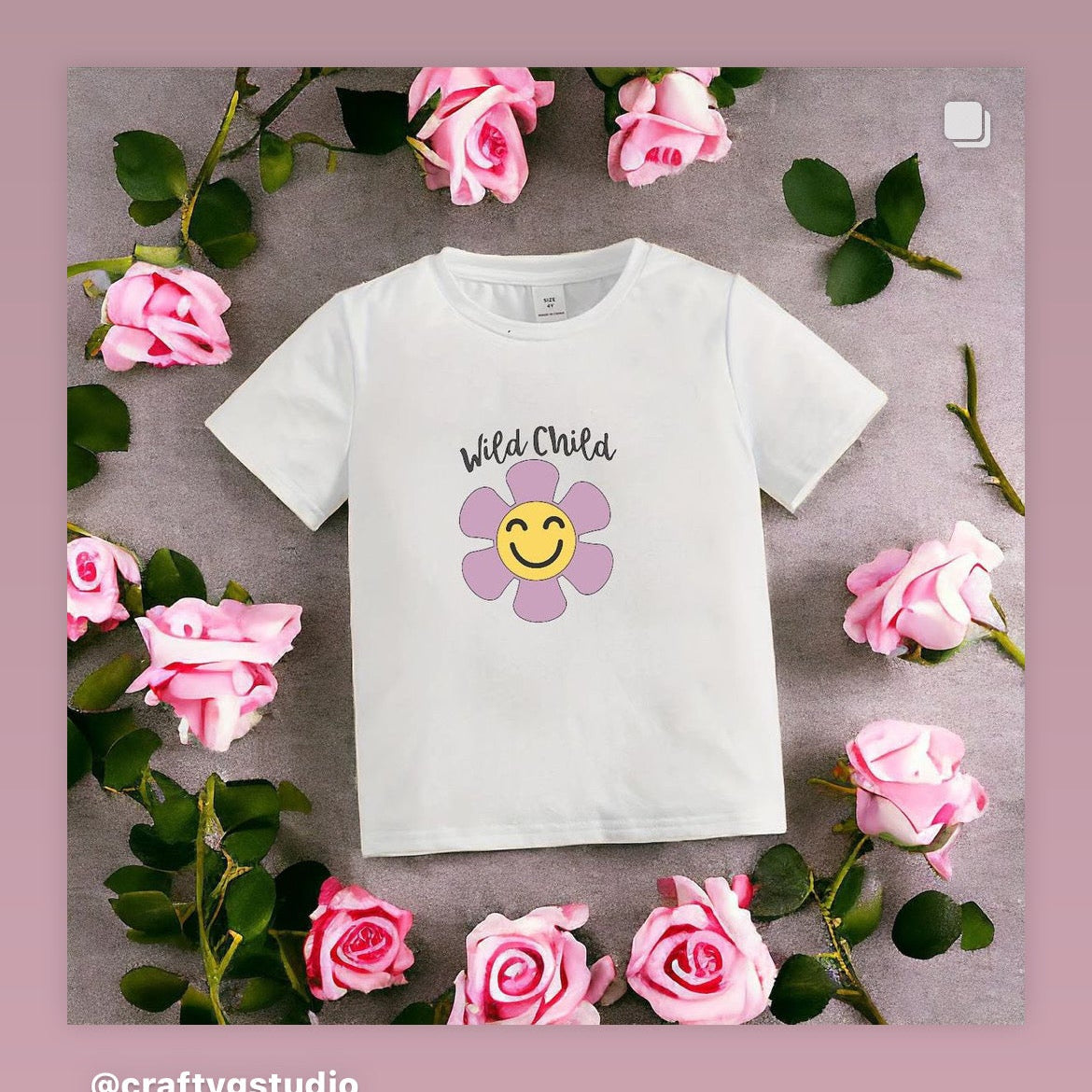 A white t-shirt with a floral design and the text 'Wild Child' on it, presented on a background with pink flowers and leaves.