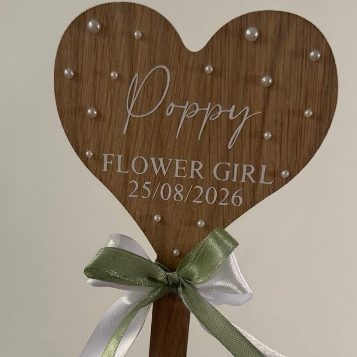 Wooden heart-shaped flower girl stick with engraved text and ribbons on a plain background