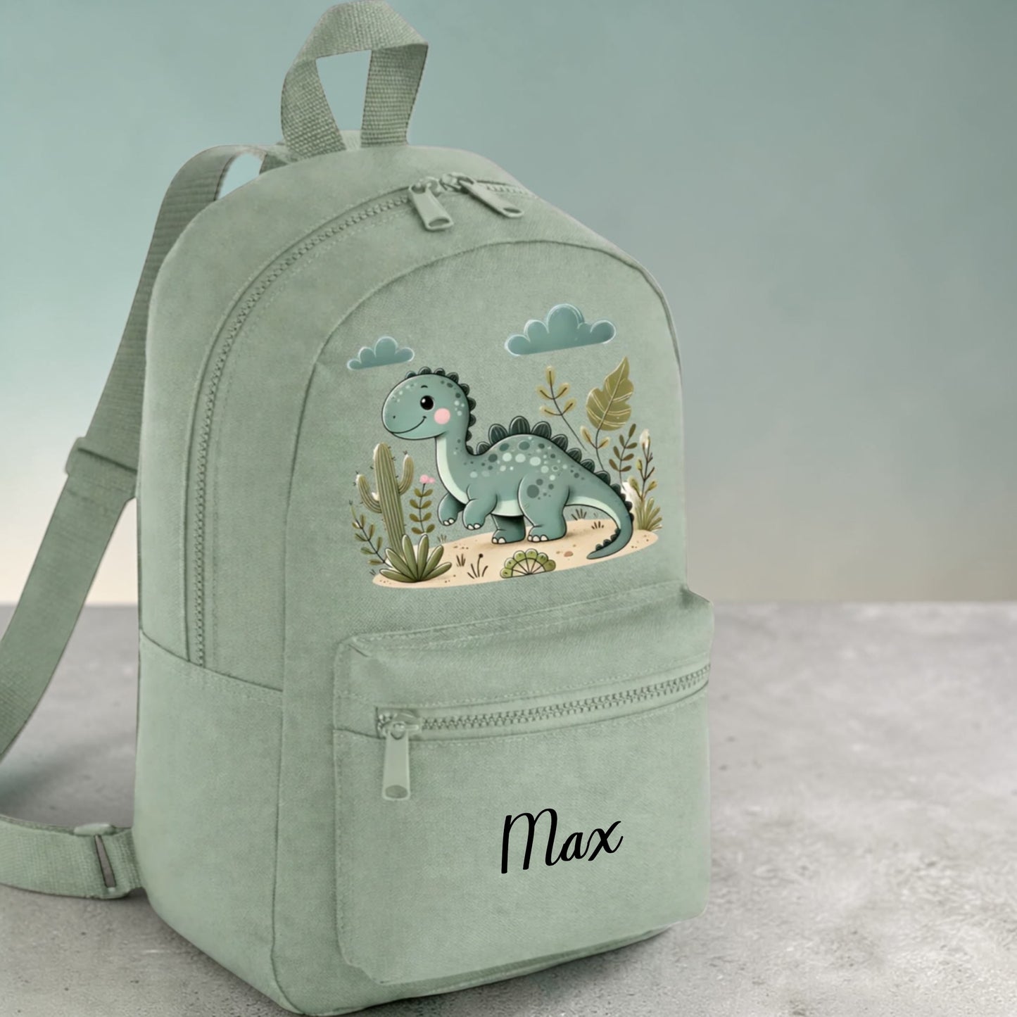 Green backpack with dinosaur design and 'Max' text on a light gray background