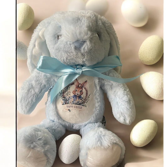 A plush toy resembling a Easter bunny, primarily in blue color, with a decorative bow and a personalized name tag.