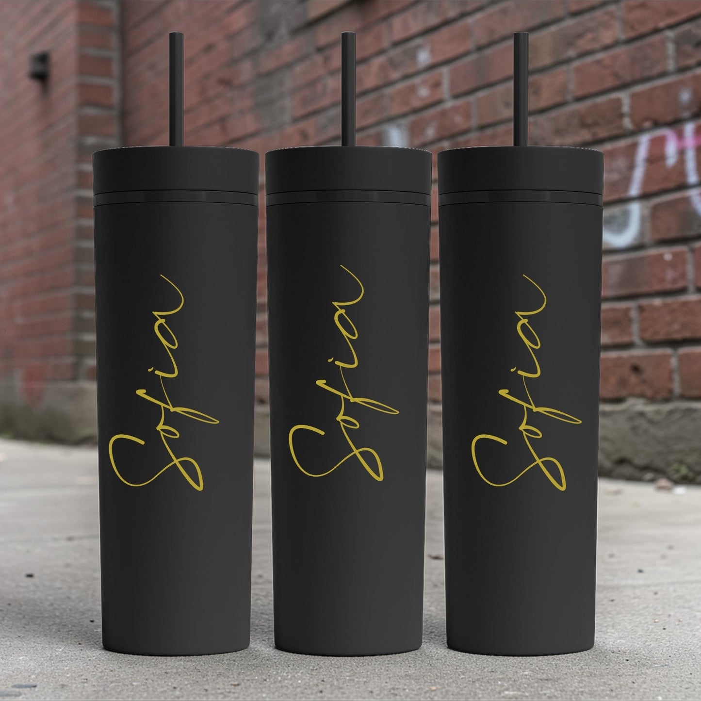 Three black tumblers with gold 'Sofia' text against a brick wall background