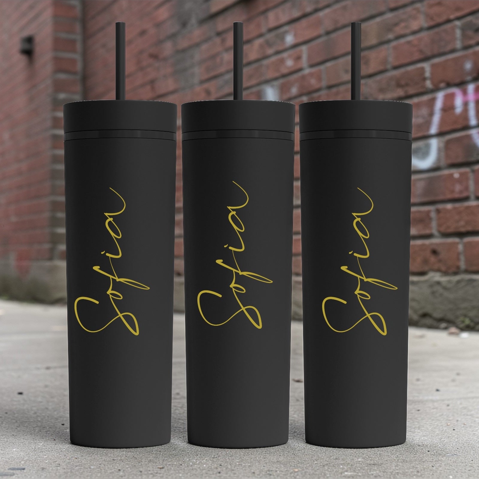 Three black tumblers with gold 'Sofia' text against a brick wall background