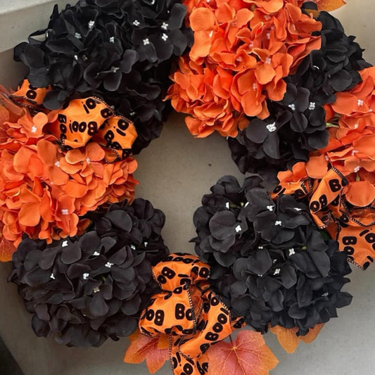 A Halloween wreath with orange and black flowers and ribbons, designed for festive decoration.