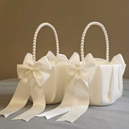 Two white flower girl baskets with pearl handles and large ribbons on a neutral background