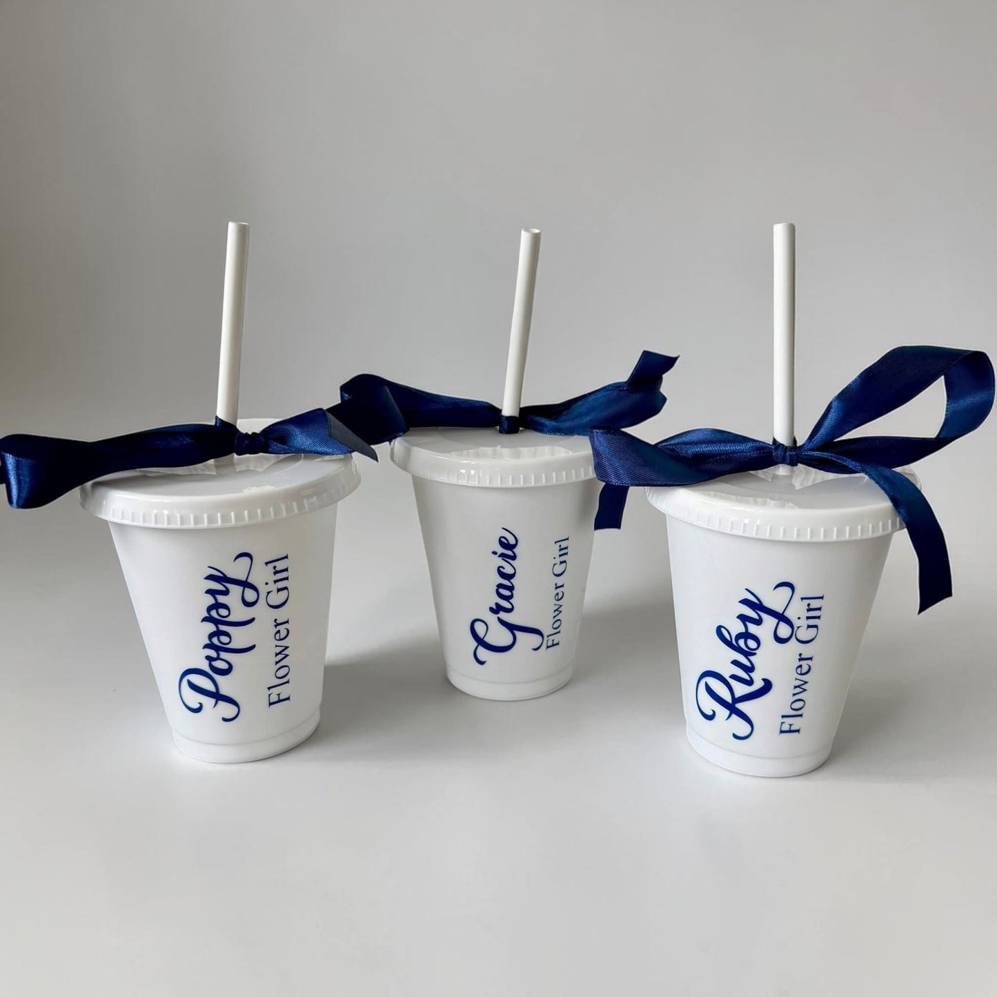 Three white cups with blue ribbons and personalized names on a gray background