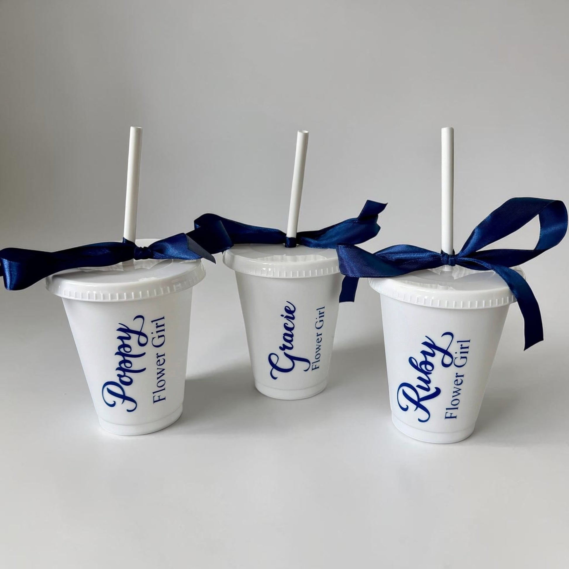 Three white cups with blue ribbons and personalized names on a gray background